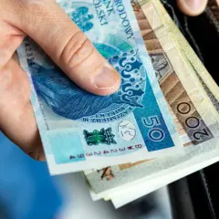 Dłoń trzyma polskie banknoty: 50 zł i 200 zł. Zastanawiasz się, ile kosztuje akt zgonu?