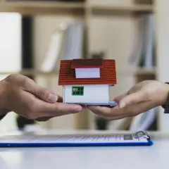 Dwie dłonie przekazują sobie miniaturowy dom. Symbolizuje to automatyczne przyjęcie spadku i przekazanie majątku.