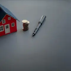 Model domu, stos monet i długopis symbolizują umowę przedwstępną sprzedaży nieruchomości wzór.