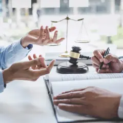 U notariusza trwa zmiana umowy dożywocia. Dwie osoby omawiają dokumenty, obok młotek sędziowski i waga sprawiedliwości.