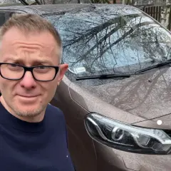 Mężczyzna w okularach przed brązowym vanem, gotowy do podpisania umowy komisu.