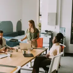 Zespół dyskutuje przy stole, czy umowa zlecenie przedłuża się automatycznie. Kobieta prezentuje coś na laptopie.