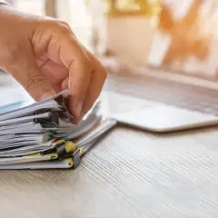 Dłoń przegląda stos dokumentów, szukając informacji, jak uzyskać odpis aktu urodzenia.
