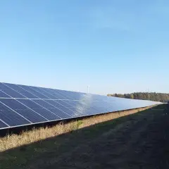 Panele słoneczne i wiatraki na tle błękitnego nieba. Dzierżawa ziemi pod farmę fotowoltaiczną to inwestycja, która może przynieść dochód.