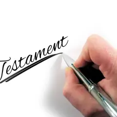 Dłoń pisze eleganckim pismem słowo "Testament", symbolizując dziedziczenie testamentowe i przekazanie majątku.