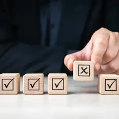 Dłoń kładzie kostkę z krzyżykiem na tle innych z zaznaczonymi ptaszkami. To symbol decyzji, jak w umowie przyrzeczonej.