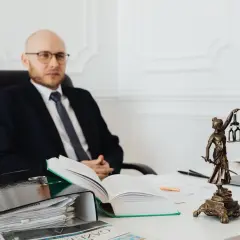 Prawnik w okularach siedzi przy biurku, obok statuetki Temidy. Zastanawia się, ile wynosi taksa notarialna.