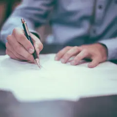 Dłoń pisze piórem na dokumencie. Czy komornik może zająć umowę zlecenie? To pytanie nurtuje wielu pracujących.