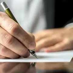 Dłoń pisze piórem umowę, która może zapewnić mieszkanie za dożywocie.