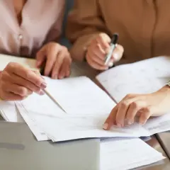 Dwie kobiety analizują dokumenty. Jedna wskazuje palcem na umowę, druga trzyma długopis. Czy notariusz zgłasza darowiznę do urzędu skarbowego?
