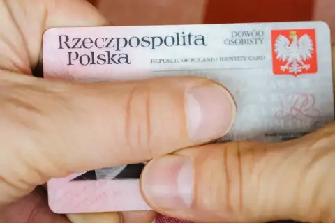 Dłonie trzymają polski dowód osobisty. Widoczny jest numer dowodu osobistego.