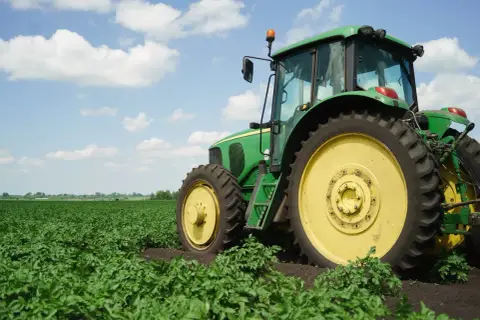 Zielony traktor na polu ziemniaków. Nowy właściciel, który nie jest rolnikiem, dziedziczy ziemię rolną i musi nauczyć się obsługi maszyny.