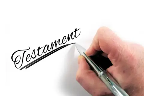 Dłoń pisze eleganckim pismem słowo "Testament", symbolizując dziedziczenie testamentowe i przekazanie majątku.