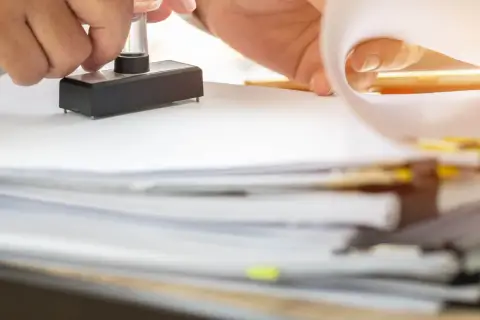 Osoba stempluje dokumenty, wśród których znajduje się nakaz płatniczy podatku rolnego.