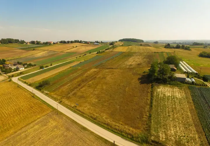 Widok z lotu ptaka na patchwork pól uprawnych, domy i szklarnie. Kto płaci podatek od dzierżawy gruntu? Rolnicy, którzy uprawiają te ziemie.