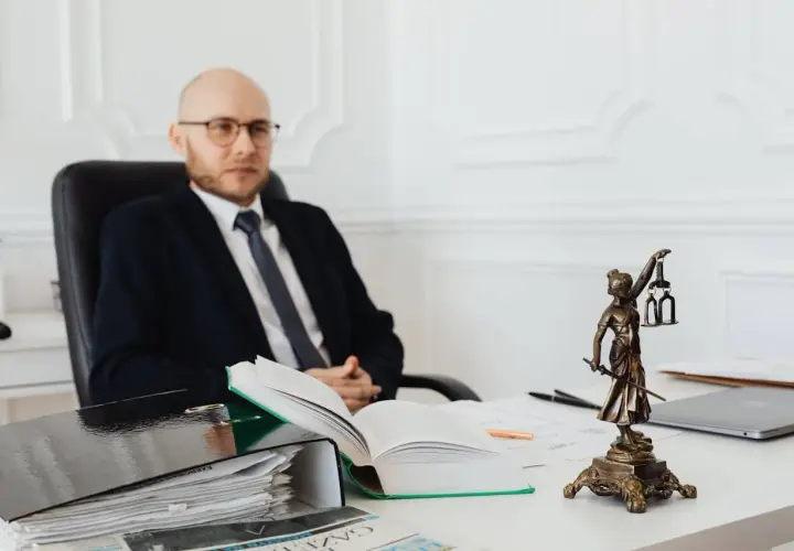 Prawnik w okularach siedzi przy biurku, obok statuetki Temidy. Zastanawia się, ile wynosi taksa notarialna.