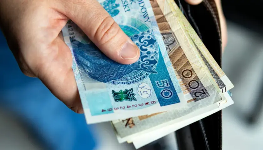 Dłoń trzyma polskie banknoty: 50 zł i 200 zł. Zastanawiasz się, ile kosztuje akt zgonu?