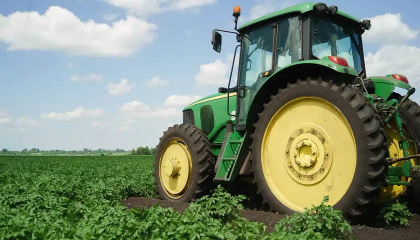 Zielony traktor na polu ziemniaków. Nowy właściciel, który nie jest rolnikiem, dziedziczy ziemię rolną i musi nauczyć się obsługi maszyny.