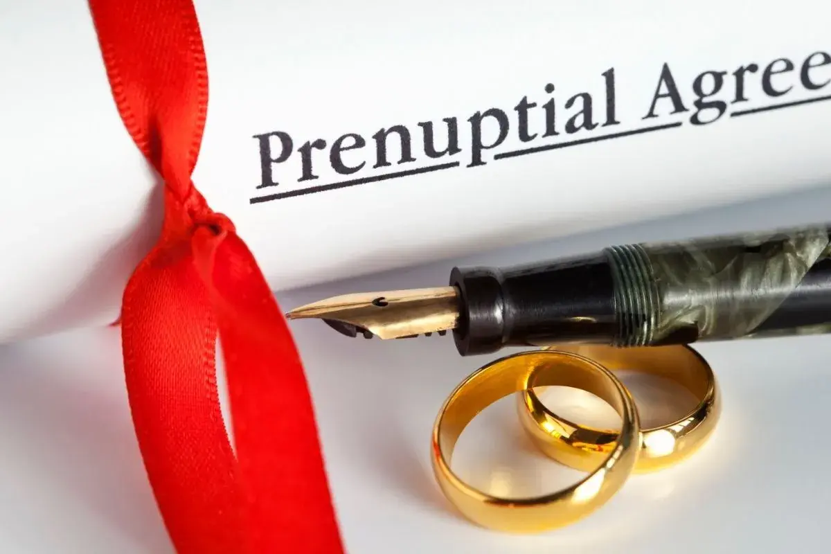 Rozdzielność majątkowa u notariusza: ile kosztuje podpisanie aktu? Złote obrączki, pióro i dokument "Prenuptial Agreement" symbolizują tę decyzję.