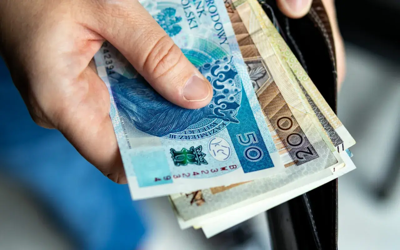 Dłoń trzyma polskie banknoty: 50 zł i 200 zł. Zastanawiasz się, ile kosztuje akt zgonu?