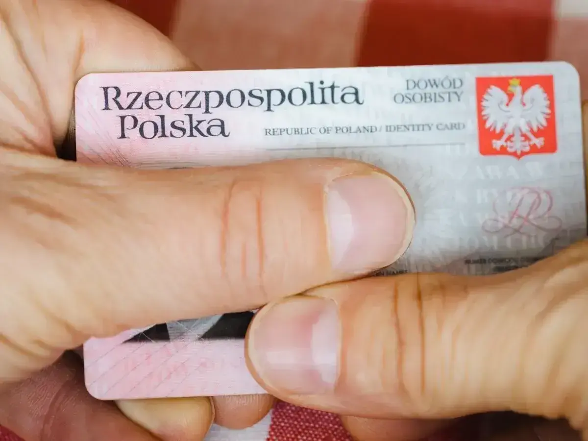 Dłonie trzymają polski dowód osobisty. Widoczny jest numer dowodu osobistego.