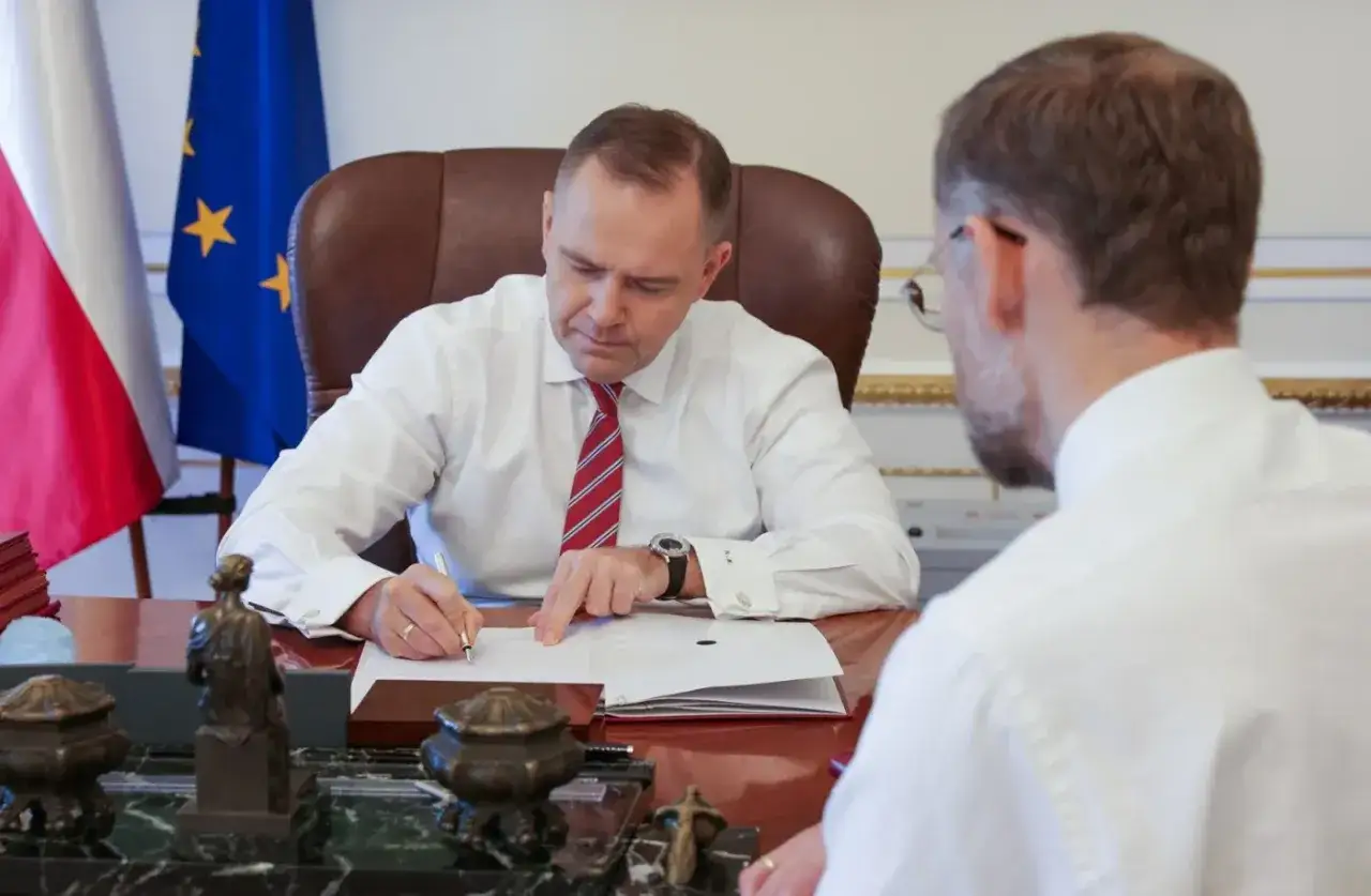 Mężczyzna w białej koszuli i krawacie podpisuje dokumenty. To ważne zlecenie.