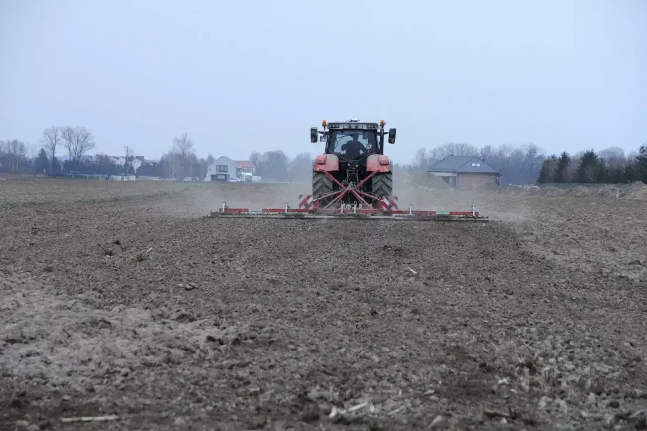 Czerwony traktor z agregatem uprawowym przygotowuje pole. To obraz przygotowań do nowego sezonu, być może związanych z nieodpłatną dzierżawą gruntu rolnego.