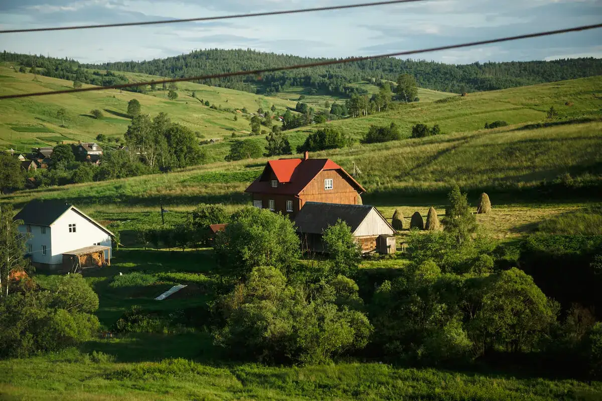 Domy na zielonych wzgórzach. Obok budynku gospodarczego, który może podlegać podatkowi, widać stogi siana.