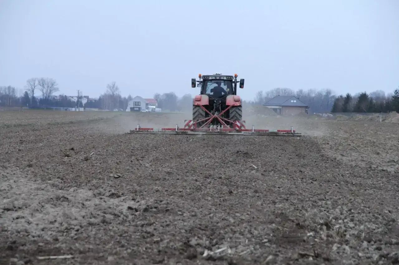 Czerwony traktor z agregatem uprawia pole. Rolnik dba o ziemię, jakby to była jego dzierżawa, choć może to być też zasiedzenie.