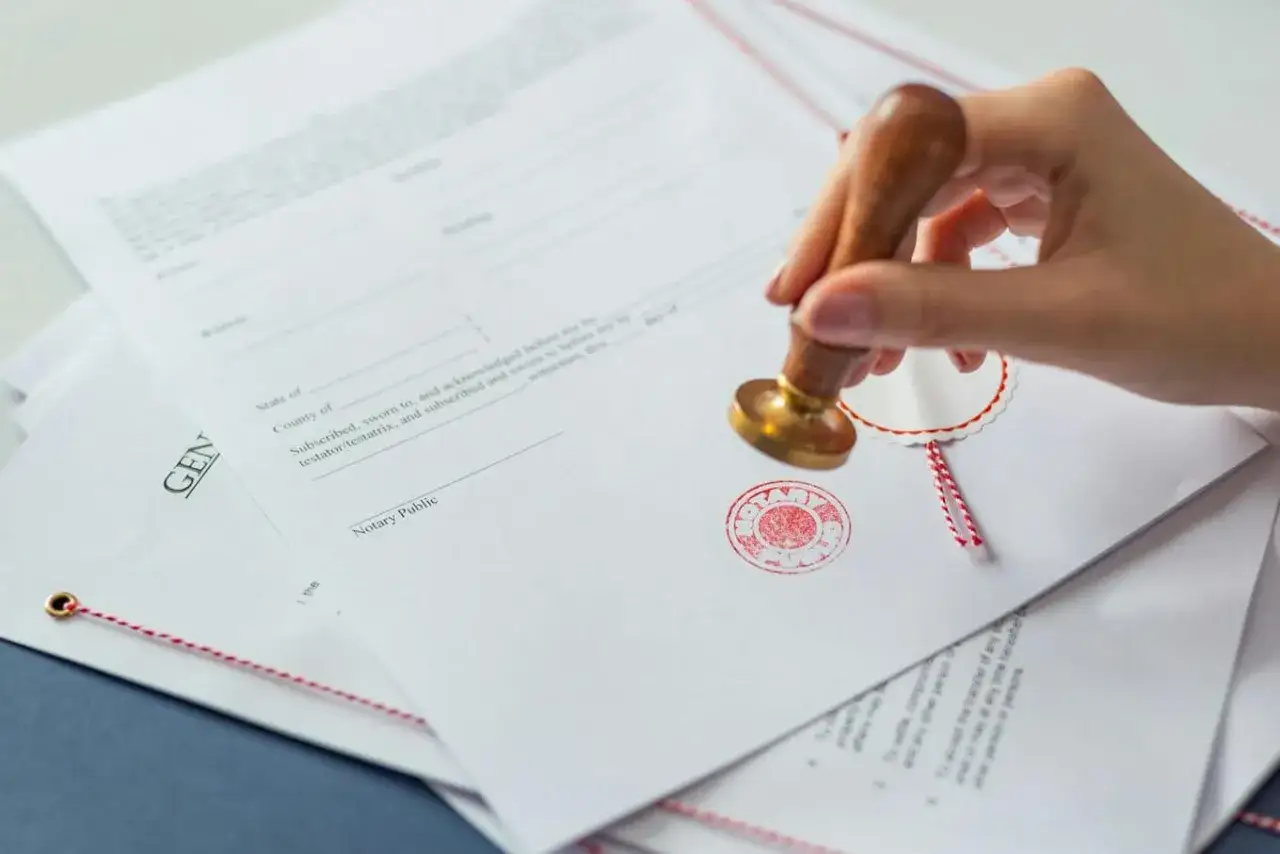 Dłoń z pieczęcią notarialną stempluje dokument, potwierdzając zgodność z oryginałem.