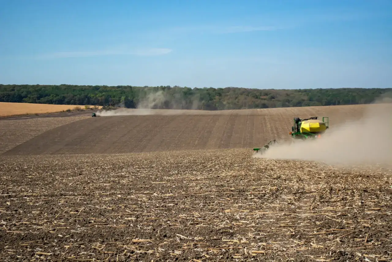 Traktor sieje na polu, tworząc kurz. To obraz ciężkiej pracy, jak dzierżawa a zasiedzenie, gdzie ziemia jest uprawiana dla przyszłych plonów.