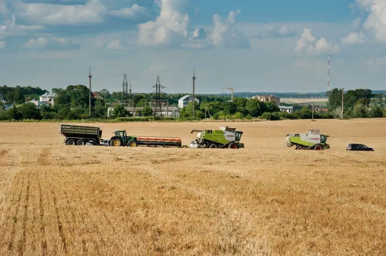 Żniwa w pełni. Kombajny i traktor z przyczepą pracują na polu, realizując umowę kontraktacji.